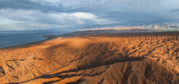 Landscape of eroded hills, badlands at sunset, Issyk Kul Lake in the background, aerial view,