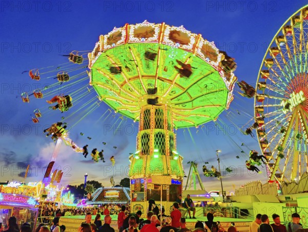 The colourfully illuminated Wellenflug chain carousel and the Ferris wheel in the evening, Cranger