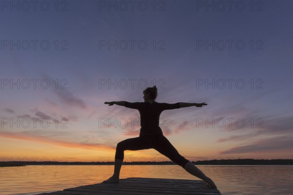 Woman practicing yoga posture Virabhadrasana II, Warrior Pose, lunging standing asana on jetty at
