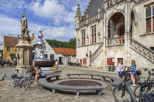 Statue of Jacob van Maerlant and cyclists in front of the Brabantine Gothic town hall in the city
