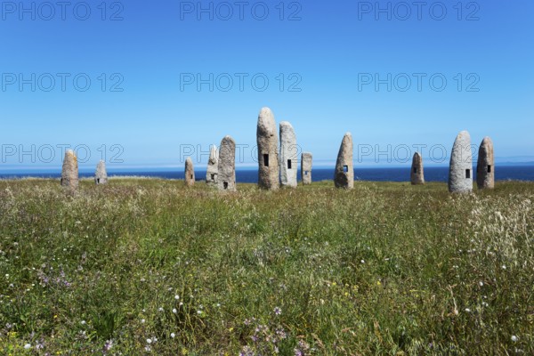 Group of standing stones in a meadow, surrounded by nature and under a blue sky with the sea in the