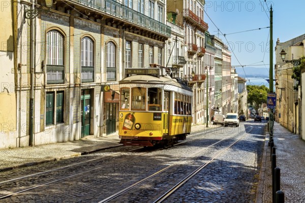 A historic yellow tram travels down a sunny Lisbon street lined with old buildings under a clear