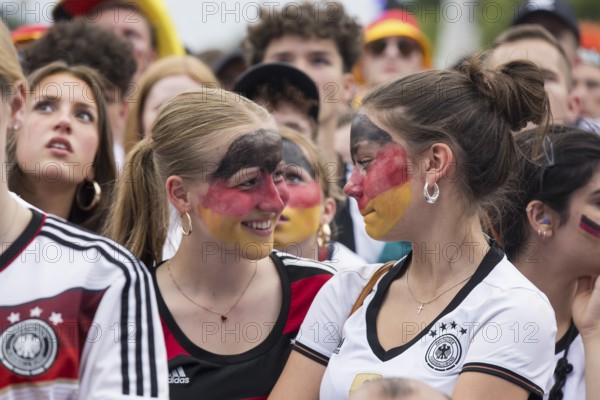 Women wearing make-up in the German national colours watch the football match in the fan zone at