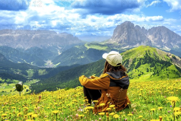 Woman hiker sitting in a vibrant flower field, admiring the stunning seceda peaks rising