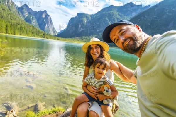 Happy family taking a selfie by the transparent water of lake dobbiaco with the dolomites in the