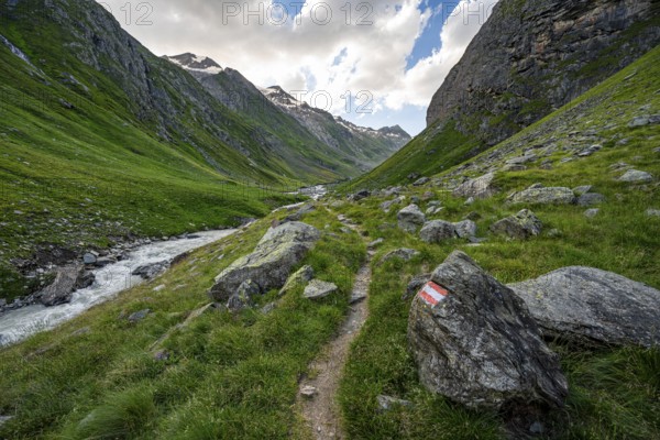 Hiking trail in the Umbaltal valley with Isel mountain stream, glaciated mountain peaks behind,