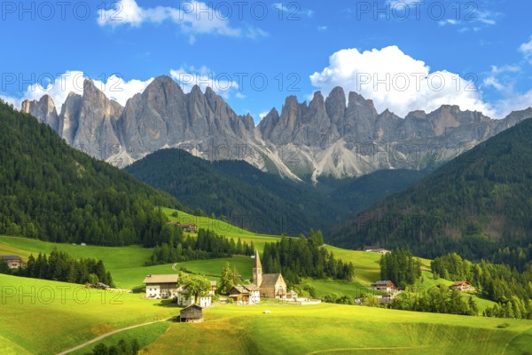 Green meadows, pine forests, and the iconic odle mountains rising majestically behind the church of