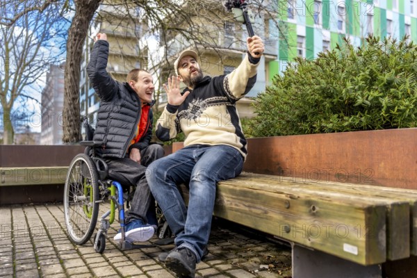 Young man in a wheelchair and his videographer friend are recording a video blog in a city park,
