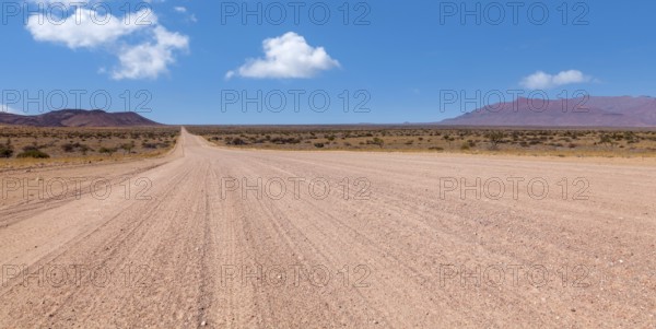 An endless desert road under a blue sky with a wide, dry landscape and mountains in the background,