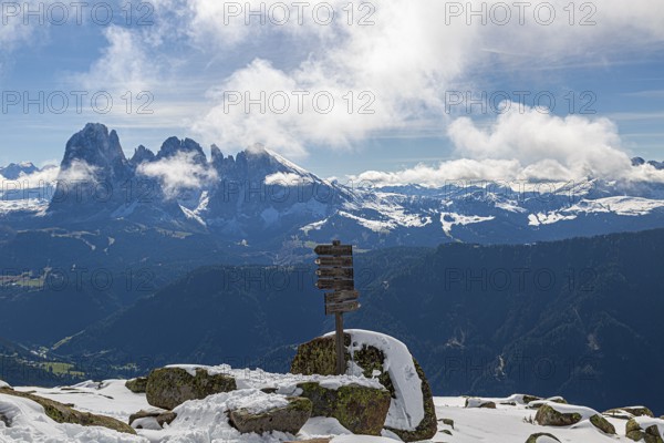 Snow-covered mountains under a blue sky with clouds and a wooden signpost with a view of the