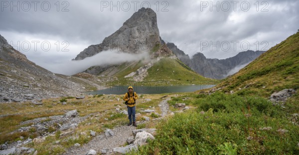 Mountaineers on a hiking trail with a view of rocky cloudy mountains and Wolayersee, hiking trail