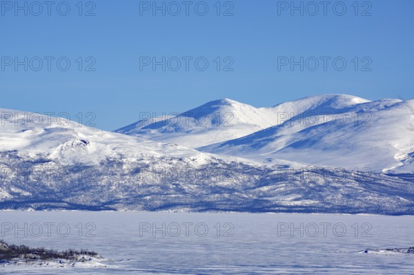 Snow-capped mountains and a frozen lake under a clear blue sky, Abisko, Abisko National Park,