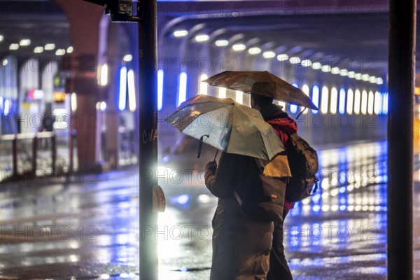 Illuminated subway at the main railway station, pedestrians at a pedestrian crossing, rainy