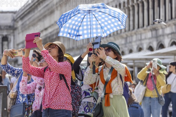 Tourists from Asia with mobile phones and parasols taking photos. Souvenir photo of St Mark's