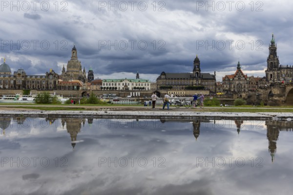 The Dresden silhouette with dark clouds behind the Church of Our Lady is reflected in a puddle on