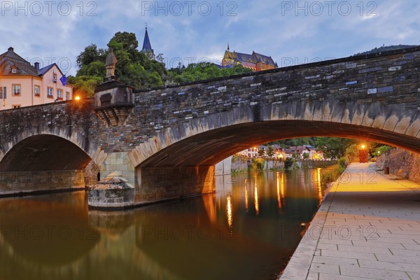 Town view of Vianden with the old stone bridge over the river Our and the castle in the evening,