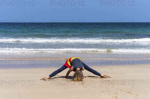 A woman doing yoga on a sandy beach by the sea. Prasarita Padottasana or forward bend with legs