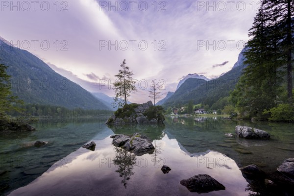 Hintersee with rocks and trees in the foreground, surrounded by mountains after sunset with
