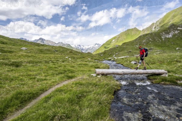 Mountaineer crossing a stream on a tree trunk, mountain landscape with mountain stream, Lasörling