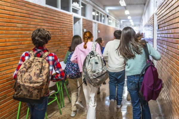 Group of students walking down school hallway between classes, carrying backpacks and rushing to