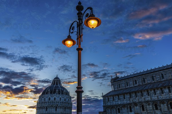 Baptistery and the Cathedral of Santa Maria Assunta at sunset under an illuminated street lamp,