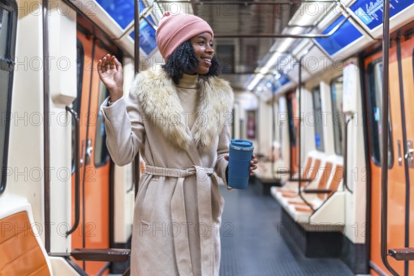 Smiling young black woman wearing winter coat and pink woolen hat holding reusable coffee cup