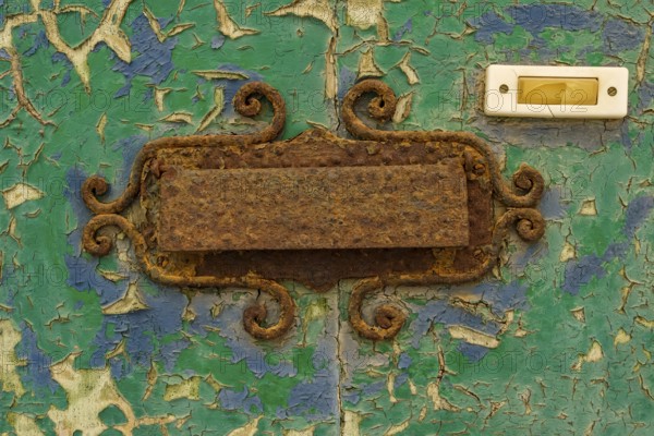 Close-up, old shabby dilapidated front door with antiquated rusty mail slot and yellowed doorbell