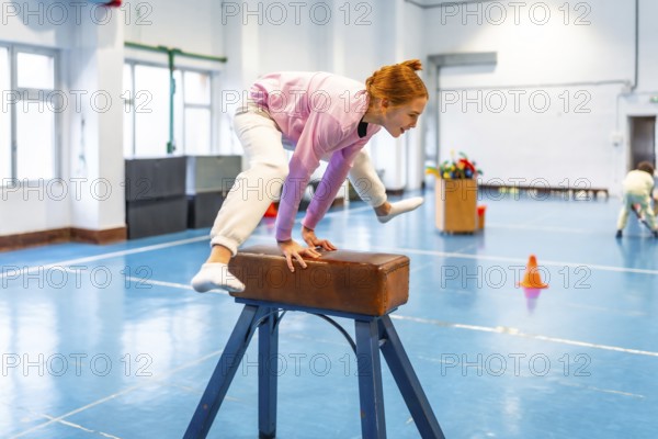 Redhead student practicing gymnastics on pommel horse, showing balance and coordination in school