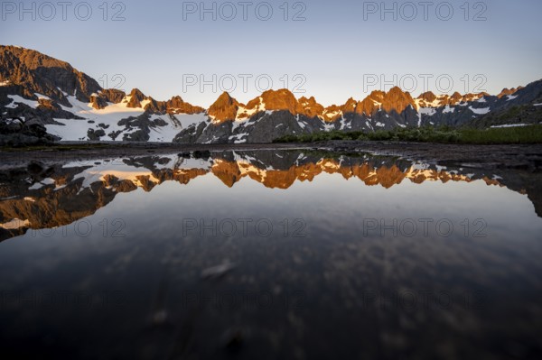 Rocky mountain peaks reflected in a small pond, mountain landscape with alpenglow at sunrise, at