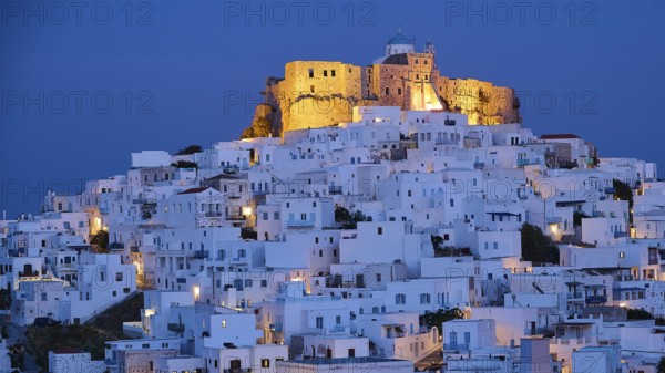 Whitewashed buildings surround an illuminated fortress under a dark blue night sky, Querini Castle,