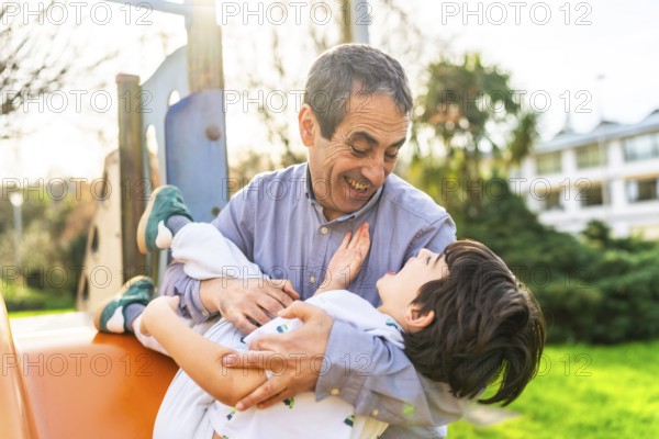 Grandfather holding his grandson and playing together at the playground, having a joyful and