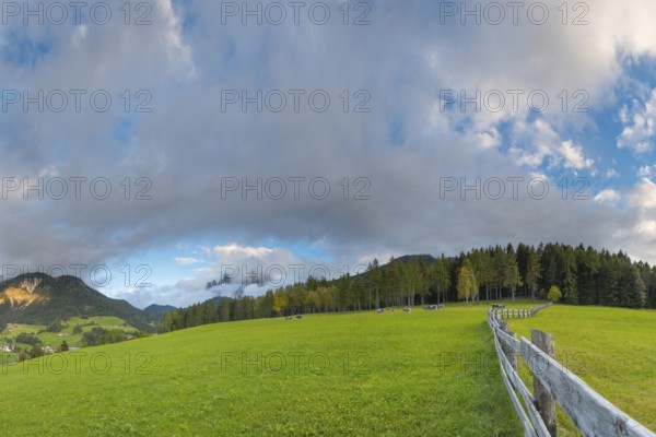 View along a wooden fence across a pasture to the mountains in the evening light, Dolomites, Odle