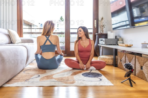 Two fitness trainers recording online yoga and meditation class in their living room using a