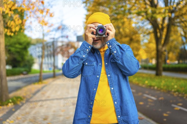 Frontal portrait of a mature modern man photographing in the city while visiting it in autumn