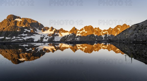 Rocky mountain peaks reflected in a small pond, mountain landscape with alpenglow at sunrise, at