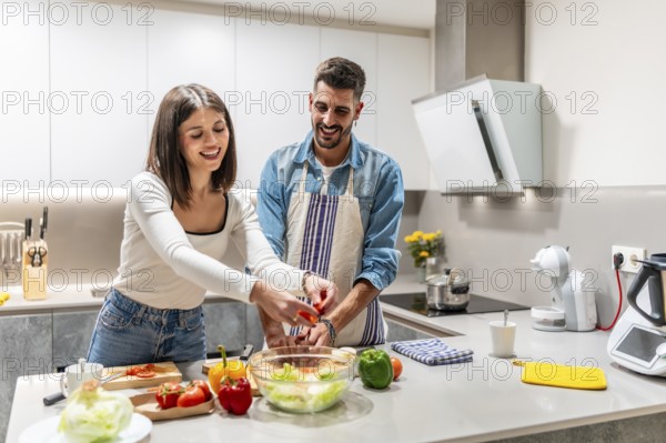 Young couple smiling and joyfully preparing a vibrant, healthy salad together in their modern