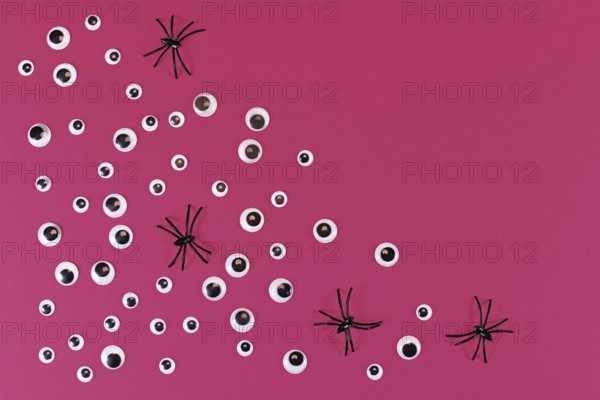Halloween flat lay with lots of spooky googly eyes and plastic spiders on pink background with