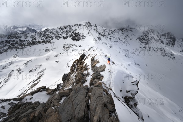 Mountaineer descending the narrow ridge of Piz Laviner, view of mountain panorama in wintry