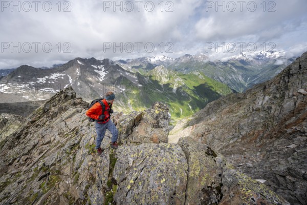 Mountaineer on a steep rocky ridge, at the summit of Lasörling, view of mountains of the Venediger