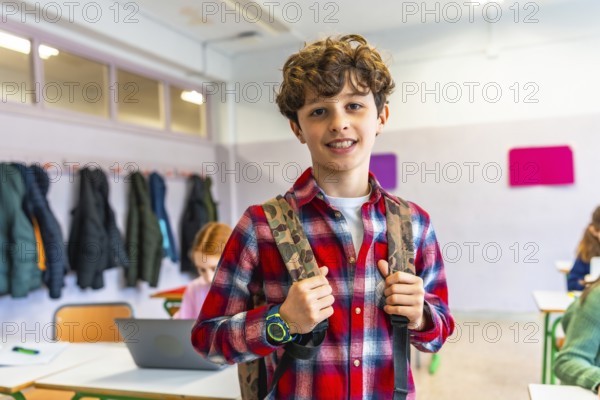 Portrait of a smiling preteen student wearing backpack in a classroom with classmates studying on