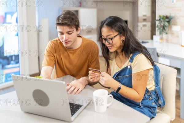 Multiethnic couple using a laptop and a credit card, making online purchases together in their