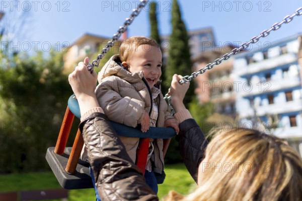 Happy little boy enjoying time on a swing while his mother lovingly pushes him in a vibrant