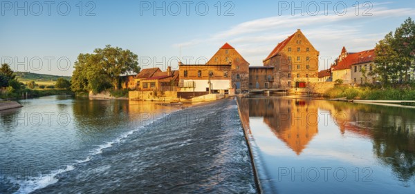 Historic watermill reflected in the river Unstrut with weir in the evening light, Laucha,