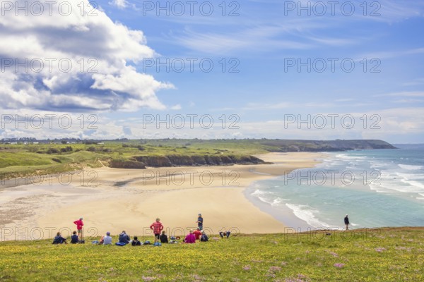 Group of hikers resting on a meadow with a scenics view at a sand beach with breaking waves and a