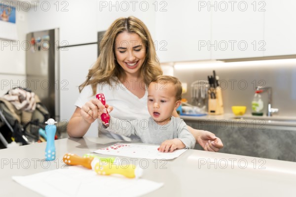 Smiling mother and baby boy having fun drawing together with colorful dot markers in a modern