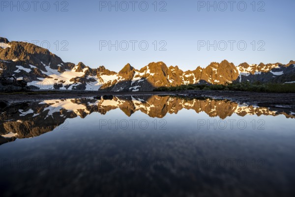 Rocky mountain peaks reflected in a small pond, mountain landscape with alpenglow at sunrise, at