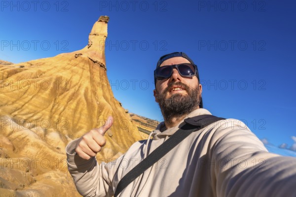 Tourist taking a selfie and gesturing thumbs up in front of a sandstone peak in bardenas reales