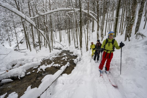 Three ski tourers in snowy winter forest with mountain stream, Hachelbach in Josefstal,