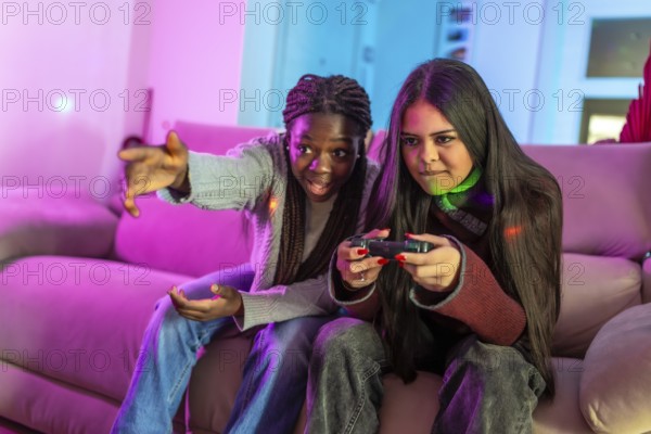 Two focused female students enjoying a gaming session on a cozy sofa at home, sharing laughter and