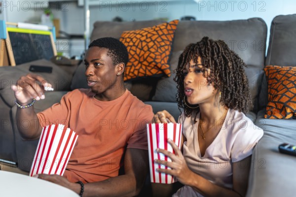 Relaxed couple enjoying a movie night at home, sitting on the floor in front of their sofa and